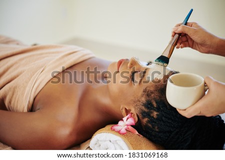Close-up image of beautician applying deep clearing clay mask on face of Black young woman Royalty-Free Stock Photo #1831069168