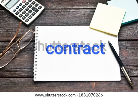 CONTRACT. The word CONTRACT is written on a light notebook near glasses, a calculator on a wooden background. Business concept. Flat lay.