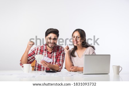Focused Indian young couple accounting, calculating bills, discussing planning budget together using online banking services and calculator, checking finances