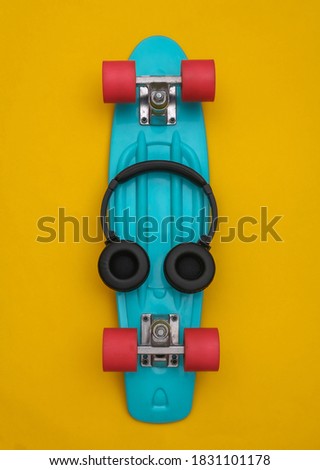 Flat lay composition of youth hipster accessories. Cruiser board and headphones on yellow background. Top view