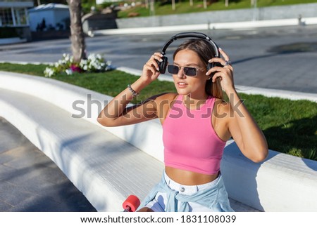 Beauty blonde woman dressed in stylish clothes and sunglasses listen music with headphones outdoors at summer bright sunny day