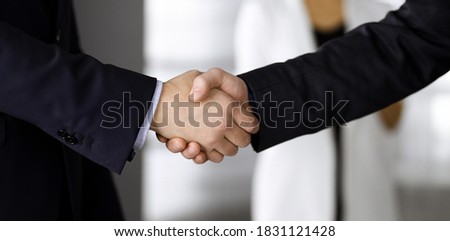 Unknown businesspeople are shaking their hands after signing a contract, while standing together in a modern office, close-up. Business communication, handshake, and marketing concept