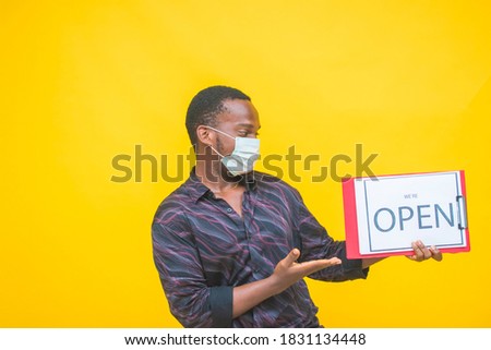 young african man wearing a medical face and holding a we're open sign.