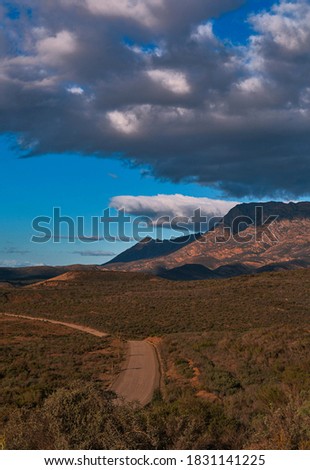 A rolling hills landscape with storm clouds looming over the mountain range in the background 