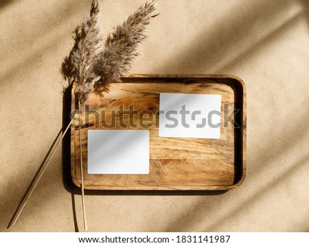 Top view of two blank paper sheet cards on a wooden tray with dry grass. Beige or sand tones. Mockup for business template, copy space.