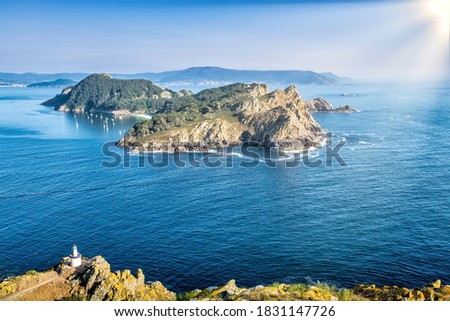 San Martiño Island seen from the top of Montefaro in the Cies Islands, Galicia, with a blue Atlantic Ocean and a sky with the sun shining and in the foreground with yellow vegetation and a lighthouse Royalty-Free Stock Photo #1831147726