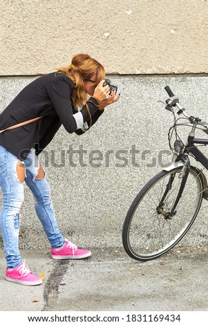 Young caucasian woman with old bicycle holding vintage camera and taking photos as a tourist in urban environment.