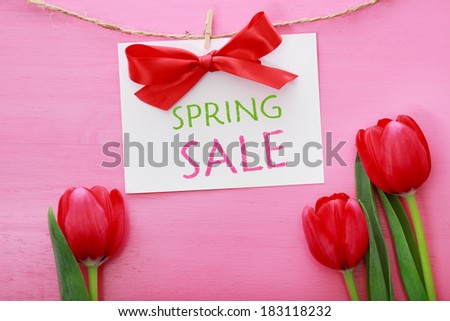 Spring sale sign hanging with clothespins over red tulips and pink wooden board