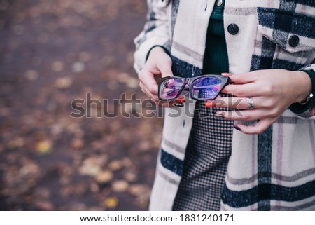 A girl in a checkered shirt is holding thick-rimmed glasses for vision correction. Close up. Autumn background. Space for text