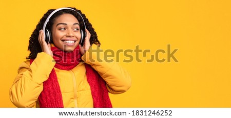 Music Lover. Cheerful African American Woman Listening To Song Enjoying Sound In Wireless Earphones Standing Over Yellow Studio Background. Winter And Autumn Playlist Concept. Panorama, Free Space