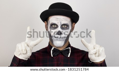 The scary clown shows the victory sign. A horrible man in clown make-up shows a victory sign to his friends.
