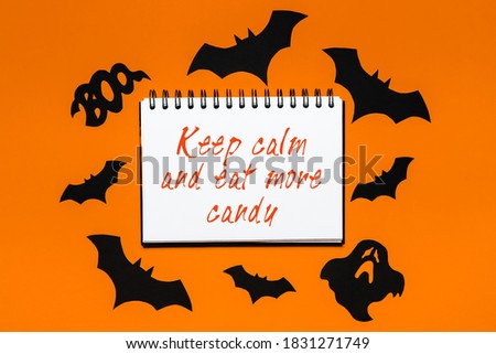 Happy halloween holiday concept. Notepad with text Keep calm and eat more candy on white and orange background with bats, pumpkins and ghosts