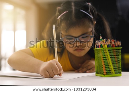 Asian girl with Down's syndrome drawing picture in art class. Concept disabled kid learning.