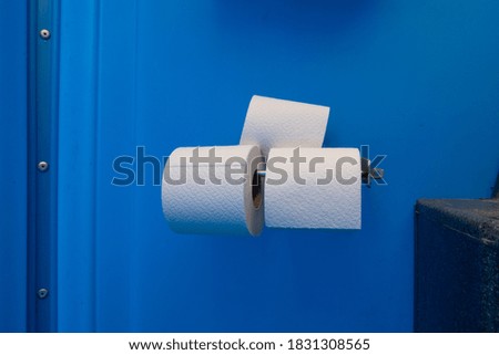 three toilet paper rolls are located on a blue wall of a mobile toilet