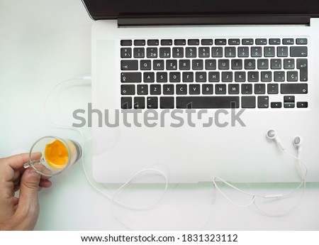 FROM ABOVE, LAPTOP WITH HEADPHONES AND HAND WITH COFFEE CUP ON WHITE TABLE