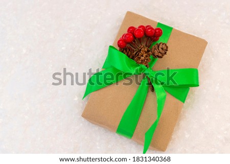 Gift wrapped in craft paper and decorated with green ribbon flat lay with snow on background. Top view picture with place for text and shallow depth of field