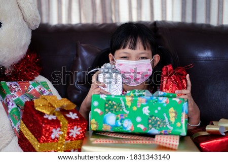 Xmas Festive asian little girl wearing face mask and holding a gift box at home