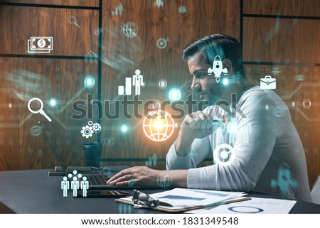 A serious caucasian analyst in casual wears, using laptop to analyze the new opportunities for international affairs in fintech. Double exposure. Research and development icons hologram.