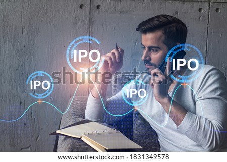 Handsome analyst in casual long sleeve talking phone, taking notes at office workplace try to analyze IPO project. Double exposure. Initial public offering hologram. Royalty-Free Stock Photo #1831349578
