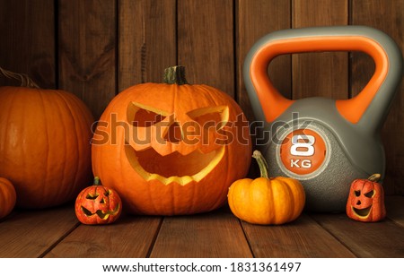 Heavy kettlebell with Halloween pumpkins on wooden background. Healthy fitness lifestyle autumn composition.