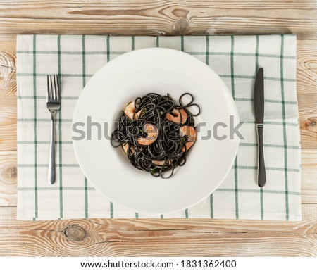 Black Italian seafood pasta with shrimps on wooden table top view. Black homemade spaghetti, noodles with cuttlefish ink, cooked sea food macaroni