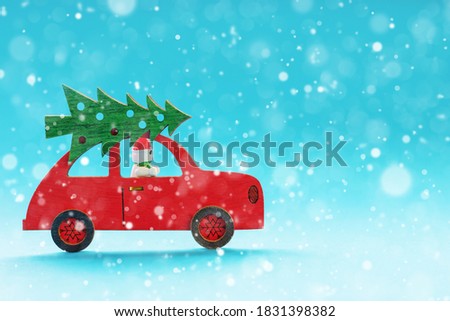 toy wooden red car with Christmas tree on the roof, snowman at the wheel and falling snowflakes on blue background, the concept of Christmas and New Year, for mockup or design, place for copyspace