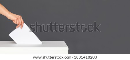 The voter holds his vote ballot paper and places it in the ballot box. Filling in ballots and casting votes in booths at polling station.The concept of free democratic vote elections. Royalty-Free Stock Photo #1831418203