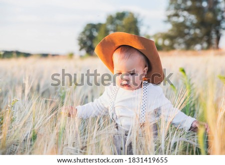 Charming baby in a cowboy costume in a wheat field on the sunset