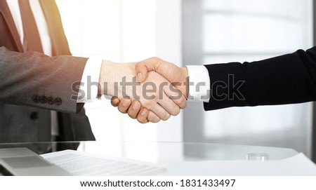 Unknown diverse business people are shaking hands finishing contract signing in sunny office, close-up. Business handshake concept