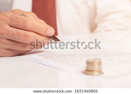 Contract signing concept. Businessman with pen over document closeup. money coins on foreground blurred, male hand in focus