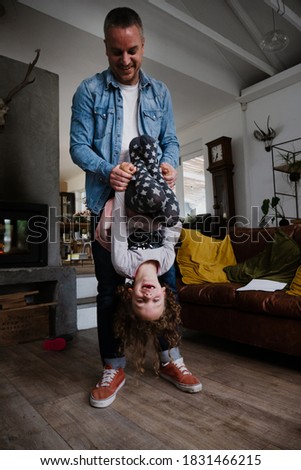 Dad and daughter bonding in living room hanging upside down with wide smile.