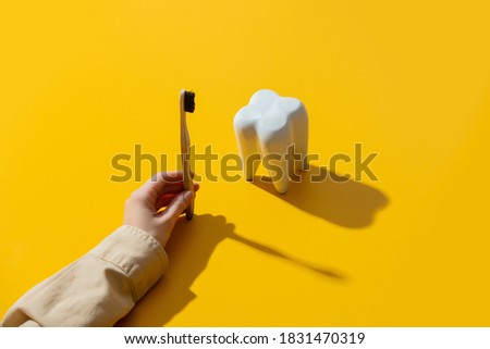 female hand brushing a tooth on yellow background 