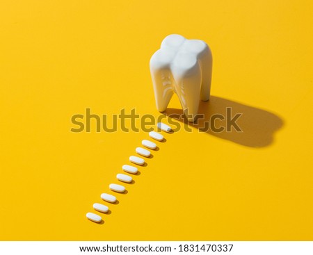 big white tooth and pills on yellow background