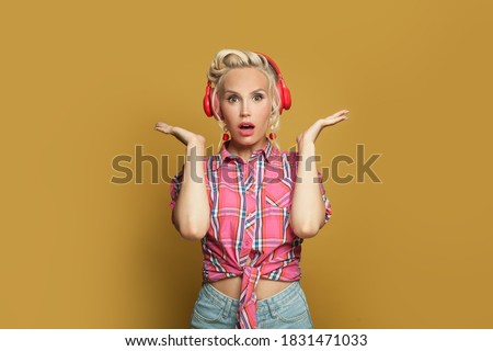 Shocked pin-up woman listening music with headphones on bright yellow background with copy space