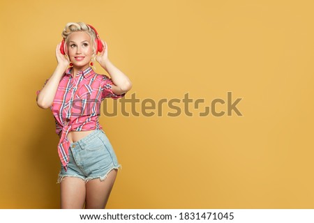 Cute pin-up woman listening music with headphones on bright yellow background with copy space