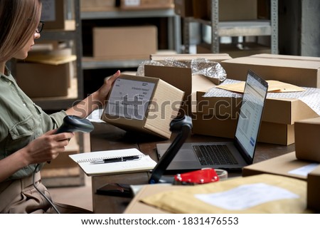 Female seller worker online store holding scanner scanning parcel barcode tag packing ecommerce post shipping box checking online retail store orders in dropshipping delivery service warehouse. Royalty-Free Stock Photo #1831476553