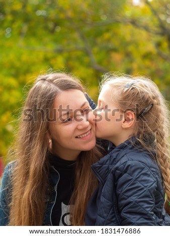 Cheerful mother and daughter smiling sitting in autumn park. Happy family walk. Cute little child playing with parent outdoors. Mother's day greeting card. Love happiness care concept.