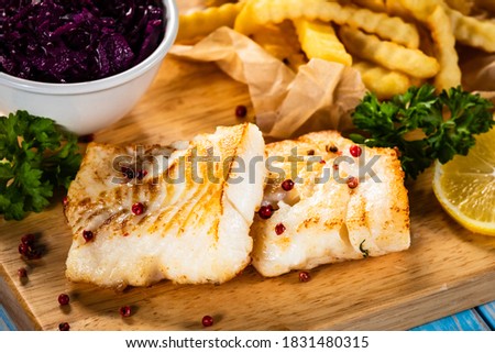 Fish dish - fried cod fillet with curly french fries and vegetable salad on wooden table 
