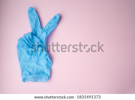 The V mark is shown with a blue medical glove on a pink background. Victory symbol. Defeating the virus. Royalty-Free Stock Photo #1831491373