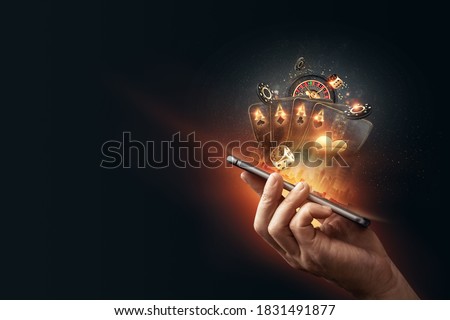 Creative background, online casino, in a man's hand a smartphone with playing cards, roulette and chips, black-gold background. Internet gambling concept. Copy space. Royalty-Free Stock Photo #1831491877