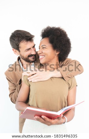 African American woman holding a book while Caucasian man hugs her from behind