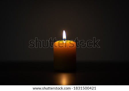 Yellow candle burning on dark background. Candle centered in the frame with empty space for text