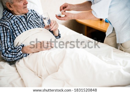 Best treatment for you. Cropped view of woman caring sick elderly man by giving pill or drug at home. Stock photo