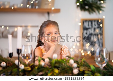 Little girl is bored sitting at the festive table on Christmas night.