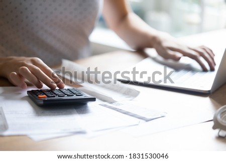 Close up young woman using calculator and computer applications, managing household expenditures, personal savings, medical insurance, education cost or taxes bills, making investments alone indoors. Royalty-Free Stock Photo #1831530046