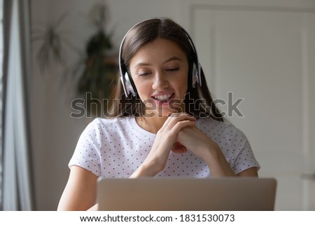 Head shot happy young pretty woman in headphones looking in laptop screen, enjoying pleasant conversation at home office. Smiling female freelancer working remotely, discussing project with client. Royalty-Free Stock Photo #1831530073