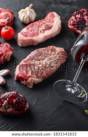 Top blade, beef steak cuts, with herbs, seasoning and red wine glass on black table, side view.