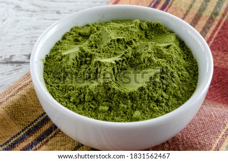 Green moringa powder in white bowl.  Horizontal composition.