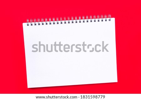 Blank white notebook sheet with a spiral on a plain red background. Concept of the New year, Christmas or Valentine day. Layout, flat lay or mockup. Copy space, place for text.