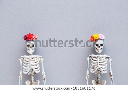 Day of the Dead and Halloween concept. Skeletons in wreaths of flowers in silver paint on a gray background.